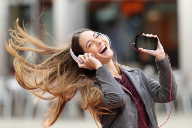 אישה צעירה ומאושרת מקשיבה למוזיקה ורוקדת ברחוב